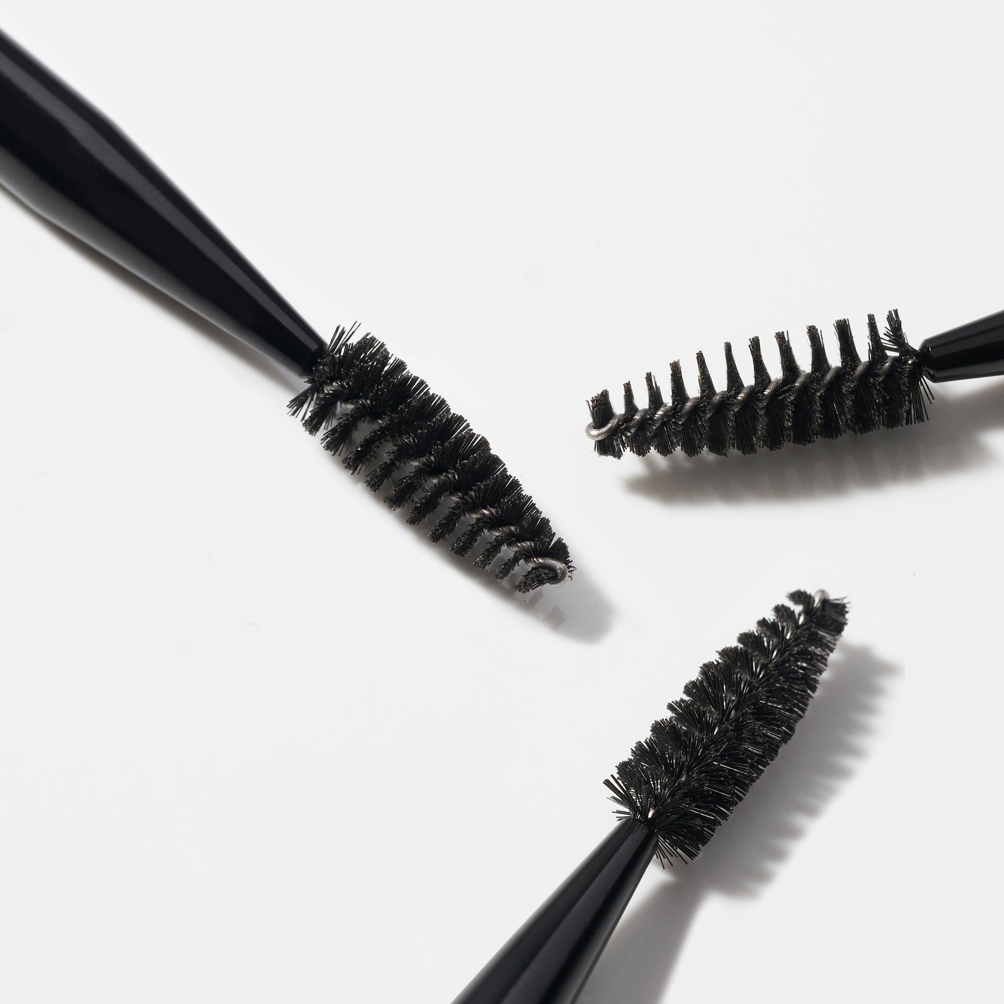 Three black brow and lash brushes with bristle heads on a white background