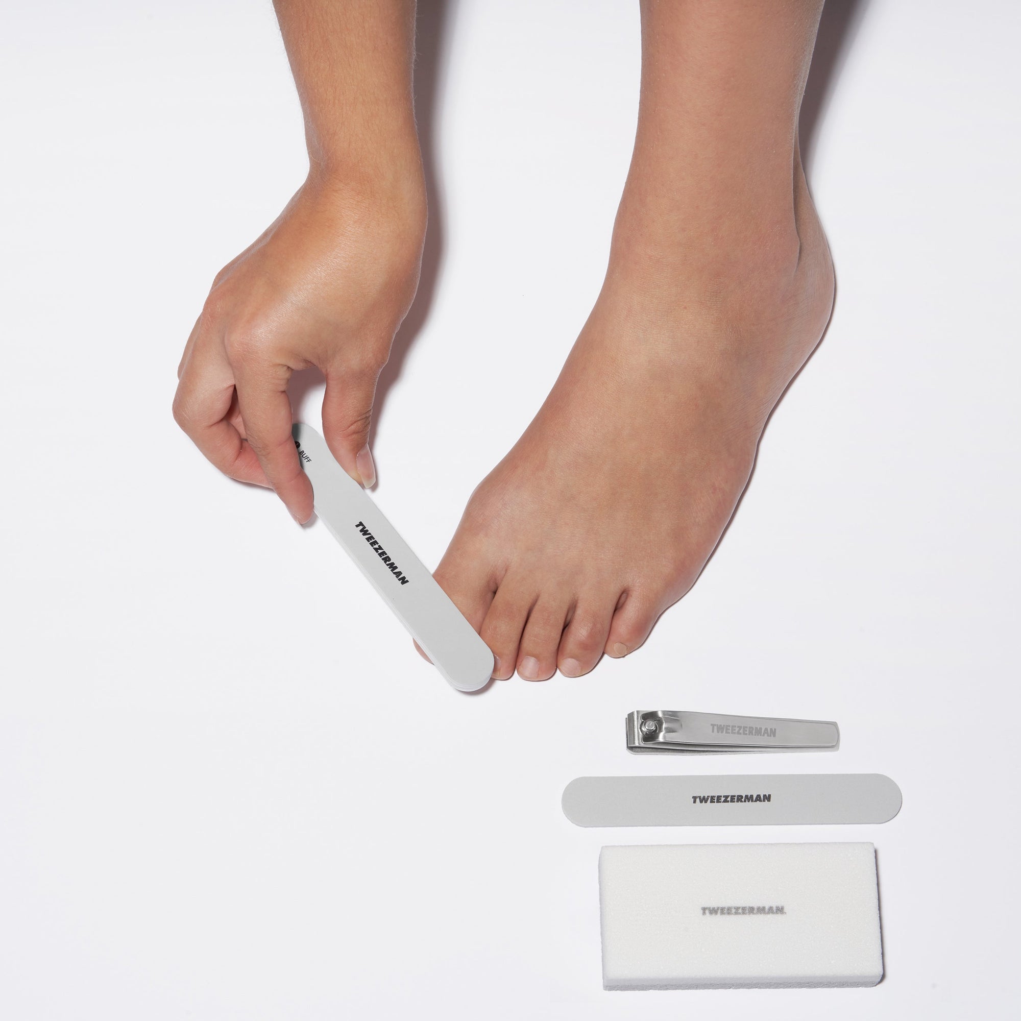 Model using Nail buffer with Toenail clipper, Nail file, and pedicure stone on side.