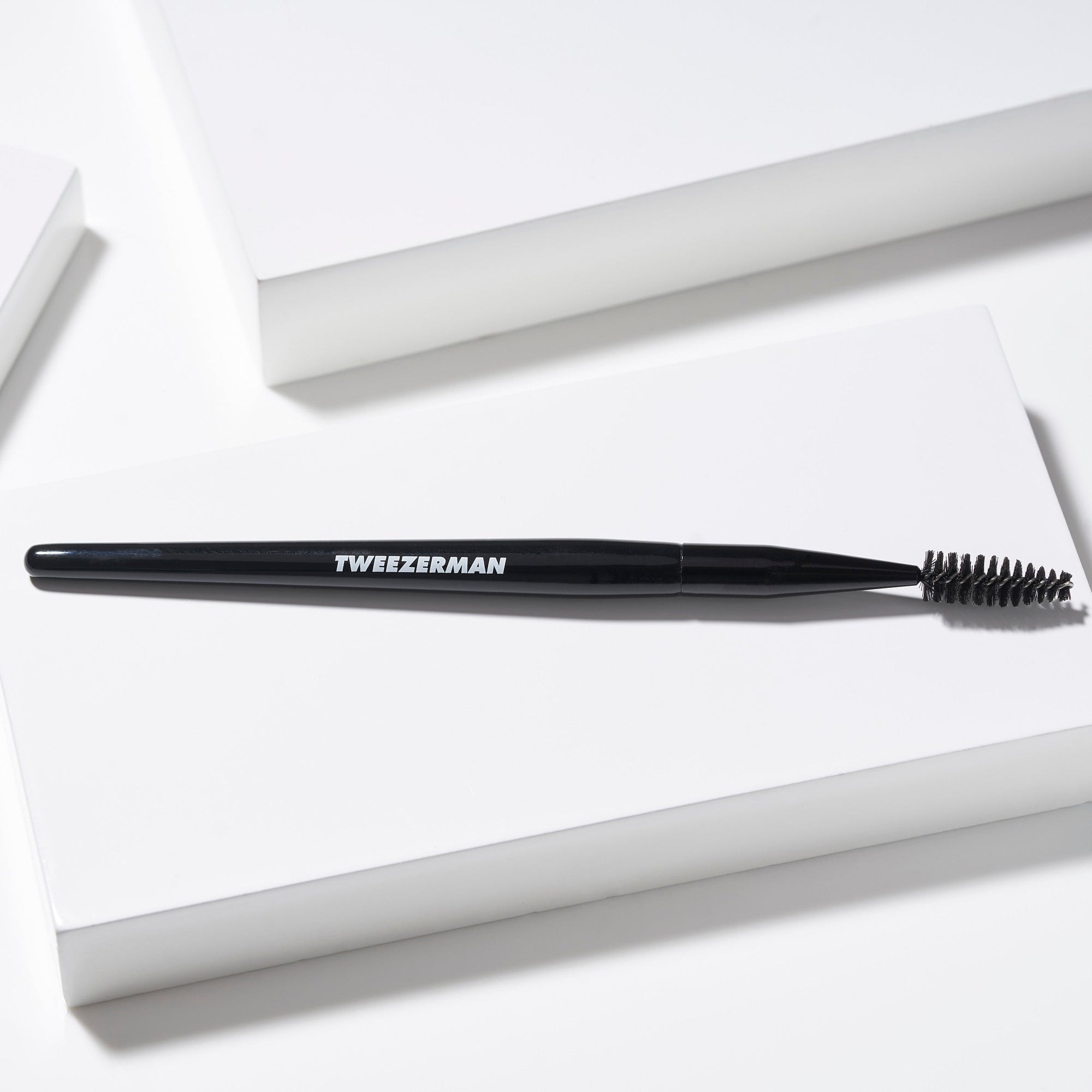 Black eyebrow brush with bristles on a white background, branded 'Tweezerman'.